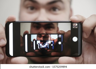 Multiplying Effect Between Two Mirror Surfaces. Re-reflection Of A Male Face In Perspective. Image In Screen Of Mobile Cell Phone. Man Portrait