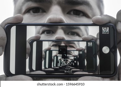 Multiplying Effect Between Two Mirror Surfaces. Re-reflection Of A Male Face In Perspective. Image In Screen Of Mobile Cell Phone. Man Portrait