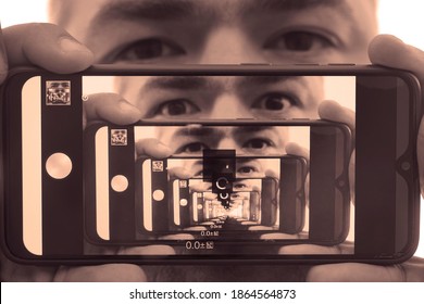 Multiplying Effect Between Two Mirror Surfaces. Re-reflection Of A Male Face In Perspective. Image In Screen Of Mobile Cell Phone. Man Portrait