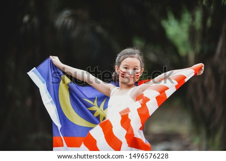 A multiracial Asian girl child holding and waving Malaysia flag. Patriotic students celebrating Independence Day. Children with facepaint. Happy and smiling on the road. Sabah Borneo. 