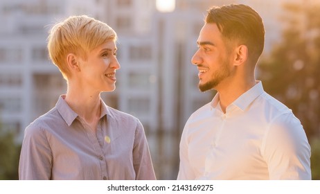 Multiracial business colleague couple arabic hispanic man and mature caucasian woman standing outdoors in sunlight talking conversation negotiation looking at camera smiling nodding heads yes positive