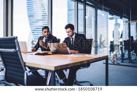 Multiracial business colleagues discussing tutorial video watching on modern laptop technology, successful male partners in formal clothes browsing banking application connecting to office internet