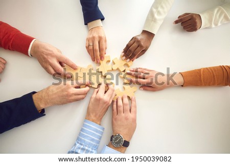 Multiracial business team assembling puzzle. Multiethnic people putting together jigsaw pieces on white table, view from above, high angle shot. Modern enterprise, teamwork, project strategy concept