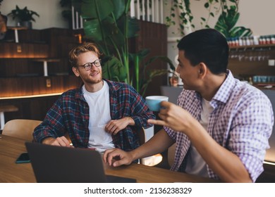 Multiracial Businessmen Looking At Each Other While Working At Table In Office Space. Concept Of Business Cooperation And Teamwork. Young Successful Men. Asian Man Drinking Tea Or Coffee From Cup