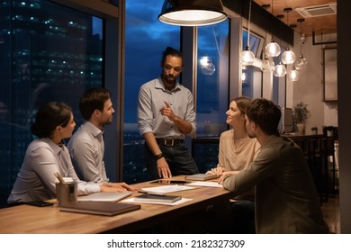 Multiracial businesspeople work in office late hours, discuss financial project at team meeting. Diverse multiethnic colleagues coworkers busy cooperate in boardroom at night. Deadline concept. - Powered by Shutterstock