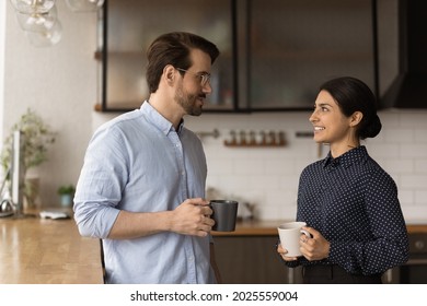 Multiracial colleagues talk during lunch break in office kitchen. Indian woman communicates with workmate hold coffee cups enjoy conversation, discuss work or personal. Good relations at work concept - Powered by Shutterstock