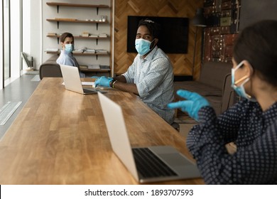 Multiracial Colleagues Wear Facial Masks And Gloves From Coronavirus Talk Work In Shared Office. Diverse Employees In Protective Gear Busy Using Computers At Coworking Workplace. Covid-19 Concept.