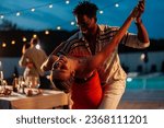 Multiracial couple, Caucasian girl and African-American guy, dancing on a poolside party by the pool, smiling and feeling in love