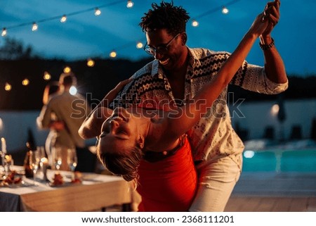 Multiracial couple, Caucasian girl and African-American guy, dancing on a poolside party by the pool, smiling and feeling in love