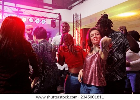 Multiracial couple dancing together while partying in crowded nightclub. Man and woman clubbing and having fun on dancefloor illuminated with spotlights at club discotheque