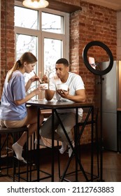 Multiracial Couple Eating At Home Kitchen During Making Eat Fast Food Video Challenge On Smartphone. Video Blogging. Man And Woman Of Generation Z Creating And Sharing Content For Social Networks