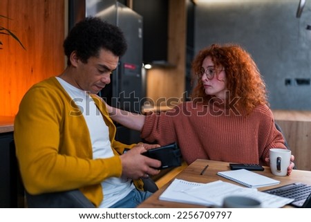 A multiracial couple has a problem with finances, they don't have enough money to meet their budget. She's comforting her boyfriend. Tablet, notebook, post it notes and papers on the table