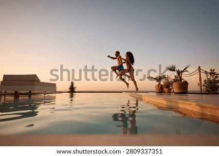 Multiracial couple having fun while jumping in outdoor swimming pool at sunset. Copy space. 