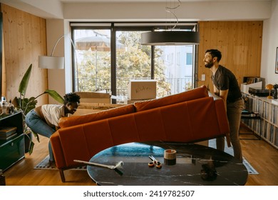 Multiracial couple helping each other while lifting sofa in living room at new home स्टॉक फ़ोटो