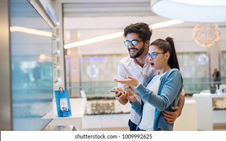 Multiracial Couple Looking At Large TV Screen At Tech Store. Buying 3D TV For Living Room. Multiethnic Couple At Shopping.