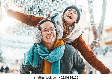 Multiracial couple in love wearing winter clothes celebrating Christmas holiday - Husband and wife having fun hanging out together walking on city street - Winter holidays and relationship concept