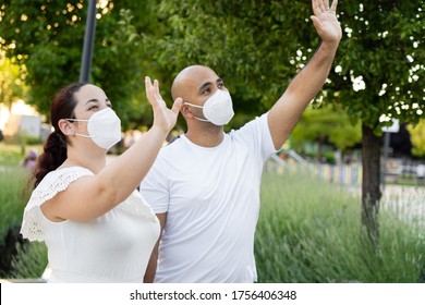 Multiracial Couple Saying Hi In The Park Smiling And Wearing Masks