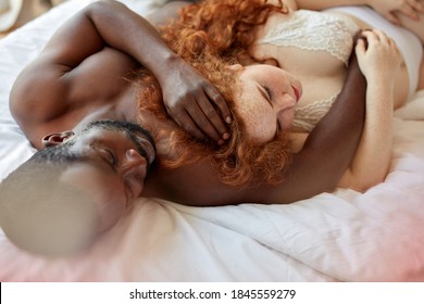 multiracial couple in sensual erotic foreplay on bed at home, half-naked afro man and redhead overweight caucasian female enjoy being together, in love, passion, people relationships