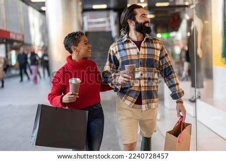 multiracial couple shopping in the city looking at window display, while carrying bags and coffee to go, valentines day