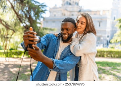 Multiracial couple taking selfie with camera in a park with city views - Powered by Shutterstock