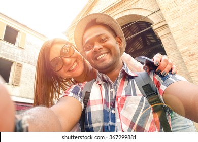 Multiracial couple taking selfie at old town trip - Fun concept with alternative fashion travelers - Indian boyfriend with caucasian girlfriend - Warm filter with powered sunlight and lens flare halo