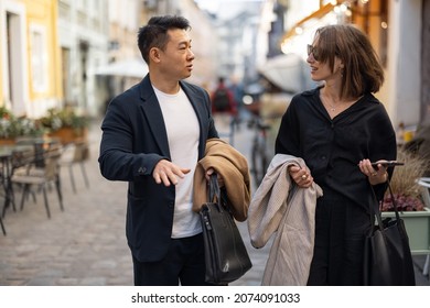 Multiracial couple walking on city street and talking. Concept of city life. Idea of friendship. Young beautiful woman with smartphone.and Serious adult asian man. Warm sunny day - Powered by Shutterstock