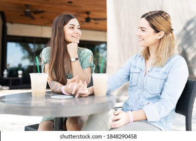 Multiracial Cute Gay Couple Sitting Outside A Coffee Shop Holding Hands, Talking And Drinking Latte