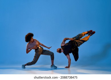 Multiracial dance couple dancing hip hop dance. Concept of contemporary dancing. Idea of choreography. Cool caucasian man and black woman on blue background in studio with shadow on floor. Copy space