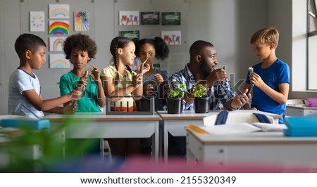 Multiracial elementary students and african american young male teacher discussing on plant in class. unaltered, education, childhood, teaching, science, stem and school concept.