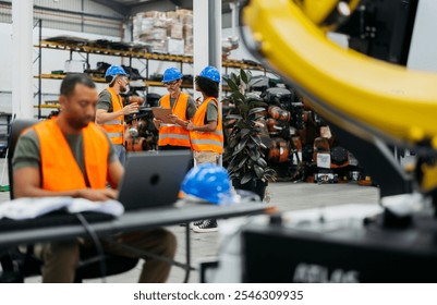 Multiracial engineers collaborating in high tech factory with robotic arms, using laptop for planning, showcasing teamwork and tech advancement in automation