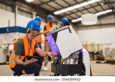 Multiracial engineers working together maintaining an agv robot in a large industrial warehouse, the senior engineer is crouching and holding a tablet while pointing at a component inside the robot - Powered by Shutterstock