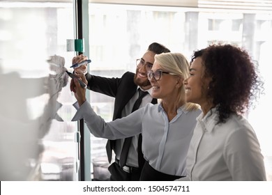 Multiracial entrepreneurs work on common task business plan strategizing together thinking on start up new ideas, team led by 50s creative manager african arabian subordinates take part use flip chart