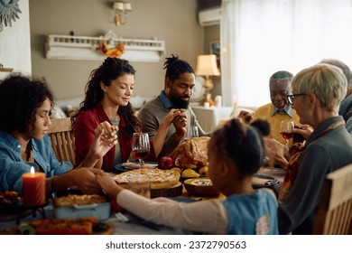 Multiracial extended family saying grace and holding hands while gathering for Thanksgiving meal at dining table. - Powered by Shutterstock