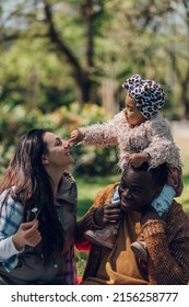 Multiracial Family Concept. Black Father And White Mother Playing With Their Daughter In The Park And Spending The Day Together. Child Playing With Flowers.