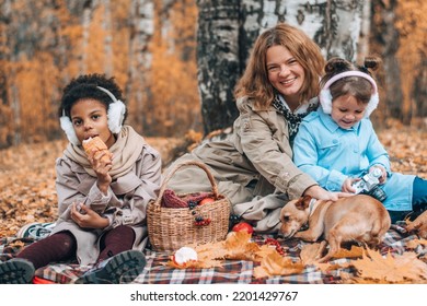 A Multiracial Family With A Dog Is Having A Picnic In The Autumn Park.Mother And Two Daughters Playing With The Dog And Having Fun.Family,autumn,diverse People Concept.