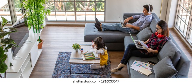 Multiracial Family, Father, Mother, And Little Daughter Stay Together At Home. Mom And Dad Working With Laptop Notebook Computer While Young Girl Does Homework. Work From Home And New Normal Concept.