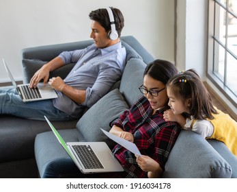 Multiracial Family, Father, Mother, And Little Daughter Stay Together At Home. Mom And Dad Working With Laptop Notebook And Teacing The Girl. Work From Home And New Normal Concept.