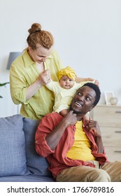 Multiracial Family Playing With Their Baby Girl On The Sofa At Home