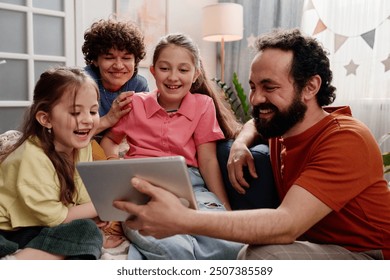 Multiracial family smiling while using a tablet on a couch with children and parents looking at screen enjoying quality time