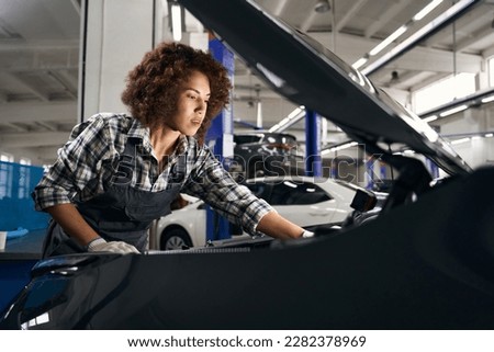 Multiracial female auto mechanic inspecting a car under the hood