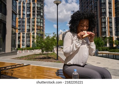 Multiracial Female Eating A Sandwich While Sitting On A Bench