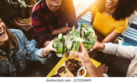 Multiracial friends cheering mojitos at bar restaurant - Young people celebrating happy hour toasting drinks and eating appetizers at tropical cocktail pub - Beverage and youth lifestyle concept - Powered by Shutterstock