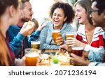 Multiracial friends drinking beer at brewery pub garden - Genuine friendship life style concept with guys and girls enjoying happy hour food together at open air bar dehor - Warm vivid filter