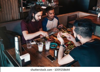 Multiracial friends eat breakfast in cafe. Young men chat while having tasty food and drinks. - Powered by Shutterstock