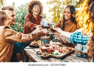 Multiracial friends having fun at barbecue dinner party in garden restaurant - Millennial people cheering red wine sitting at outside bar table - Youth lifestyle, food and beverage concept - Powered by Shutterstock