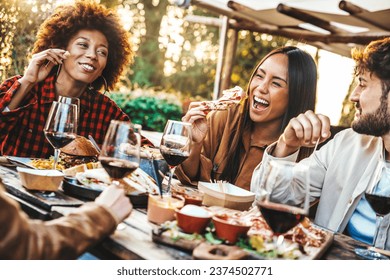 Multiracial friends having fun at barbecue dinner party in garden restaurant - Millennial people cheering red wine sitting at outside bar table - Youth lifestyle, food and beverage concept - Powered by Shutterstock