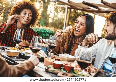 Multiracial friends having fun at barbecue dinner party in garden restaurant - Millennial people cheering red wine sitting at outside bar table - Youth lifestyle, food and beverage concept
