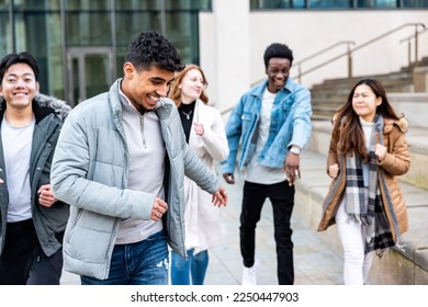Multiracial friends running and enjoying time together at city or university - Happy friendship and diversity concepts with millennial young people living a carefree lifestyle