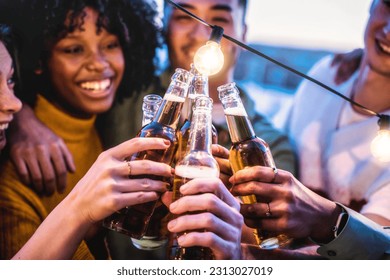 Multiracial friends toasting beer bottle at rooftop party - Young people having fun together outside - Food and beverage life style concept with guys and girls drinking alcohol on summer open bar - Powered by Shutterstock