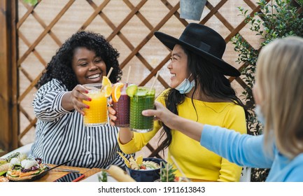 Multiracial friends toasting with fruits fresh smoothies in coffee brunch bar during corona virus outbreak